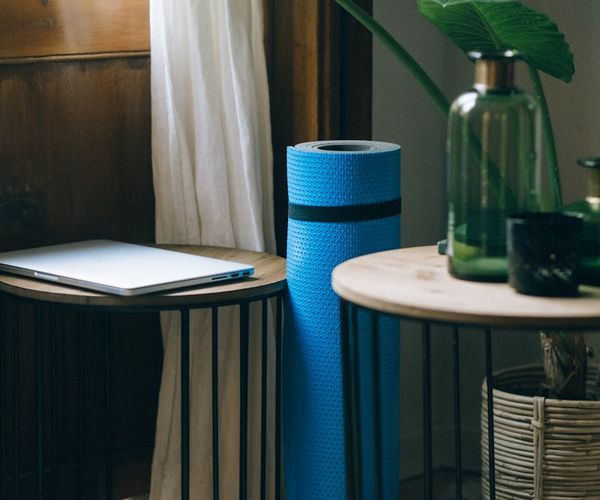A calm and tidy corner of a room with a yoga mat and a plant.